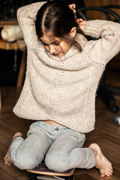 一个6岁的黑头发女孩在家里穿着毛衣，踩着滑板，拉直头发，长发，特写，情绪，蓝色的眼睛，在家里室内，彩色照片，照片为股票图片下载