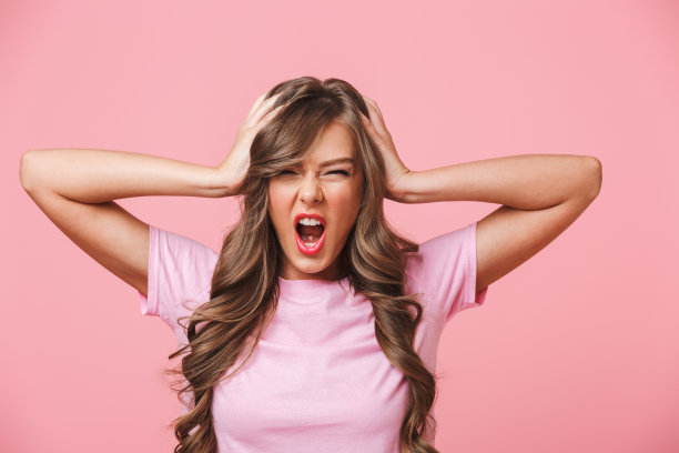 照片的特写是一个愤怒的女人，她留着长长的卷发，穿着一件基本的t恤遮住了耳朵，因为可怕的噪音而尖叫，在粉红色的背景下与世隔绝图片下载