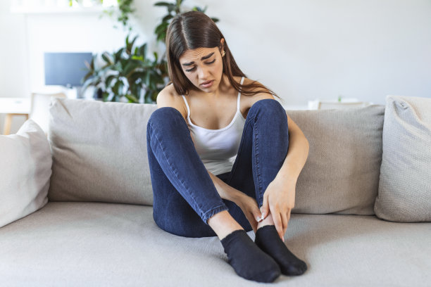 白天在家坐在沙发上，用手按摩肿胀的脚。年轻的白人妇女遭受腿部疼痛的照片。在办公室工作了一天后，女人在按摩她的腿图片下载