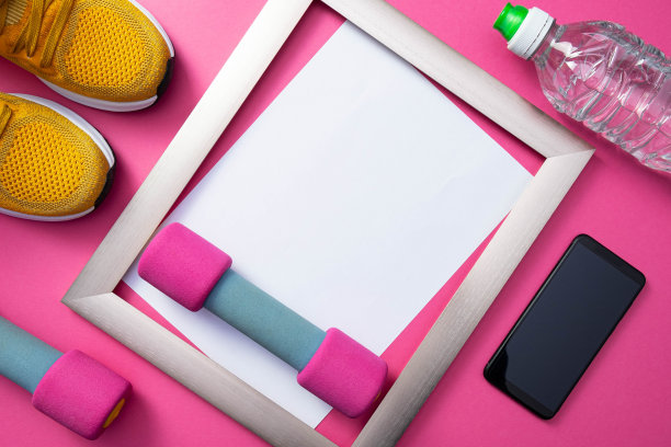 黄色运动鞋，金属框架，一部手机和一瓶水，哑铃躺在普通的粉色背景上图片下载