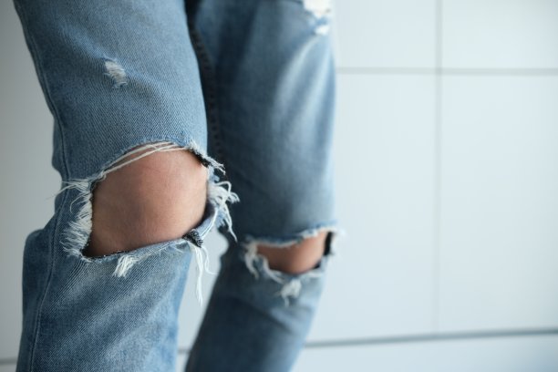 一个穿破牛仔裤的男人的特写镜头。蓝色的，陈旧的，时髦的，破旧的。在白色背景上。意大利时装图片下载