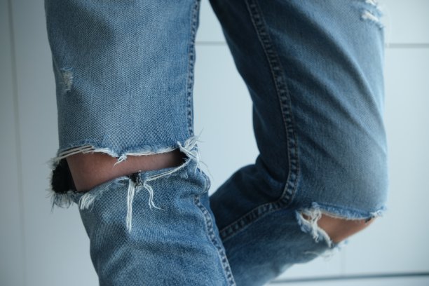一个穿着破牛仔裤的男人的特写。蓝色的，古老的，时尚的，破旧的。在白色的背景上。意大利时装图片下载