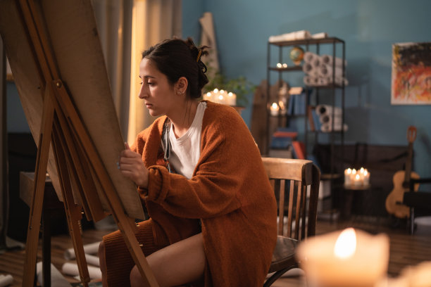 一个若有所思的女孩坐在椅子上，在家里的一个画架前，把她的思想倾注在一幅画上图片下载