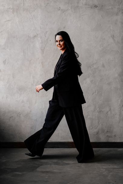 美丽而自信的女人穿着黑色长裤套装走在灰色的墙上图片下载