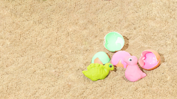 蛋壳旁边用橡皮泥制成的绿色和粉红色的恐龙。沙子的背景。孩子的玩具。最小的概念。图片下载