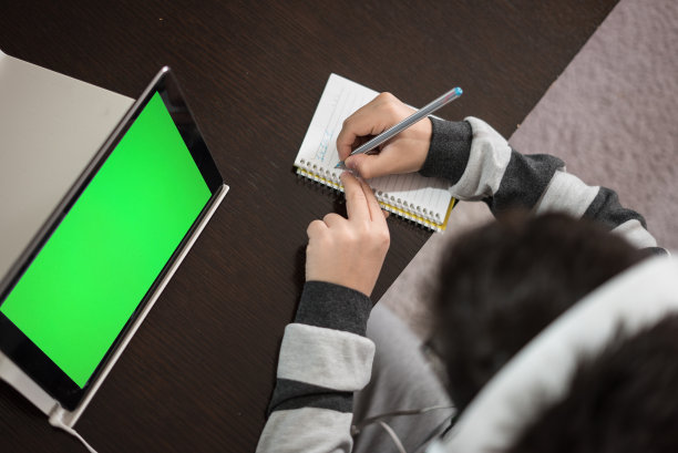 十几岁的男孩正在使用平板电脑，从家庭教育和远程学习水平照片聚焦在前面的绿色屏幕到她的手图片下载