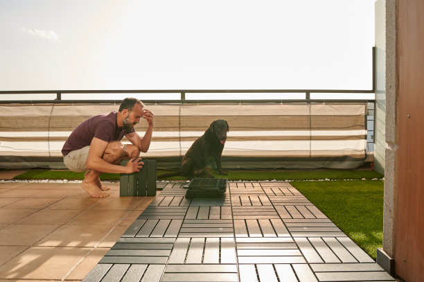 一名沉思的中年男子在他的阳台上搭建了一个人造地板，旁边坐着他的拉布拉多寻回犬图片下载