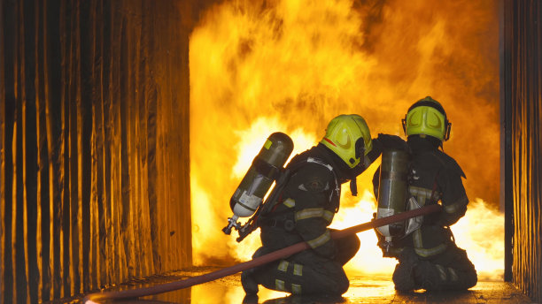 一组消防队员或身着制服的消防队员使用消防水龙带对火热燃烧的集装箱内的火灾和危险烟雾进行紧急事故救援。人。英雄团队合作。图片下载