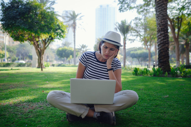 女人在公园草地上用笔记本电脑工作图片下载