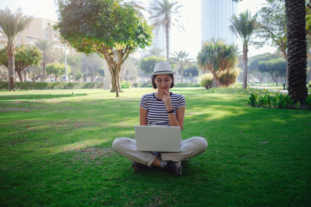 女人在公园草地上用笔记本电脑工作图片下载