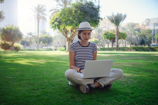 女人在公园草地上用笔记本电脑工作图片下载