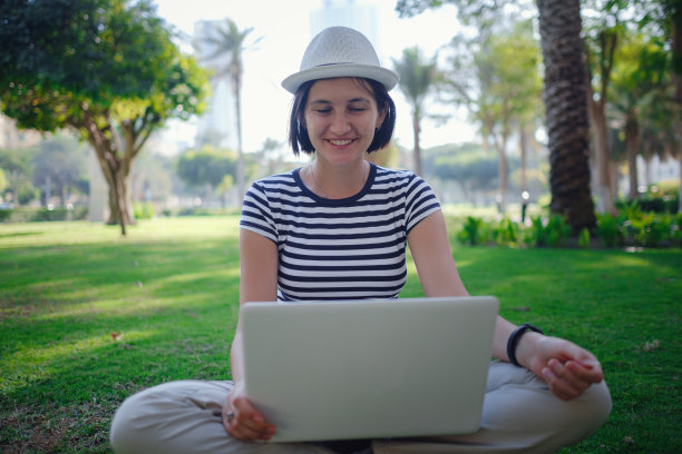 女人在公园草地上用笔记本电脑工作图片下载