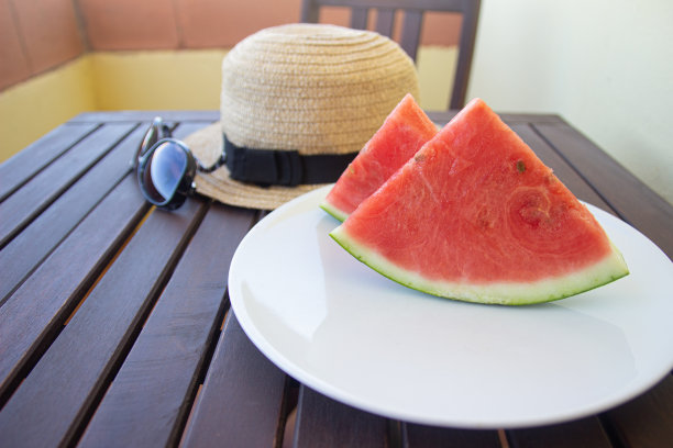 放着西瓜片、帽子和太阳镜的盘子放在露台桌上。夏天的概念。图片下载