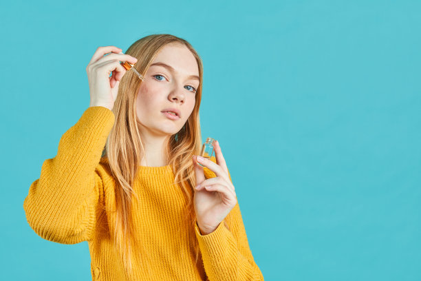 年轻女孩的肖像在她的脸上涂抹血清在蓝色的背景。图片下载