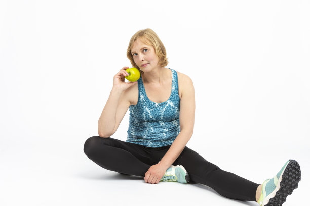 成熟的健身女运动员在慢跑装摆姿势与绿色苹果在白色。水平的形象定位图片下载