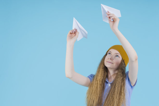 穿蓝色格子裙、戴帽子的金发少女放飞纸飞机图片下载