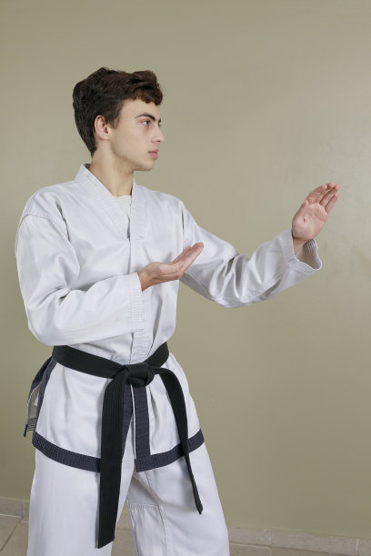 垂直图像的青少年表演双刀手的姿势。跆拳道武术中拦阻攻击的姿势。穿着白色的长袍和黑色的腰带。图片下载
