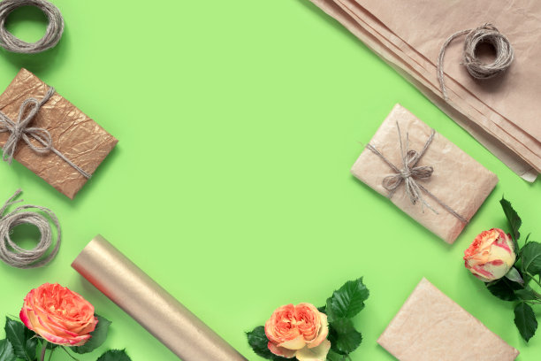 绿色背景中用绳子绑着的包装纸礼品盒和红黄色玫瑰花束图片下载