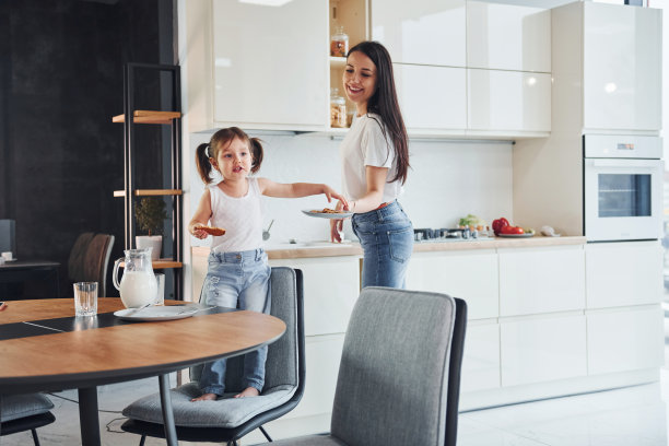 小女孩吃饼干。母亲和她的小女儿在室内厨房里图片下载