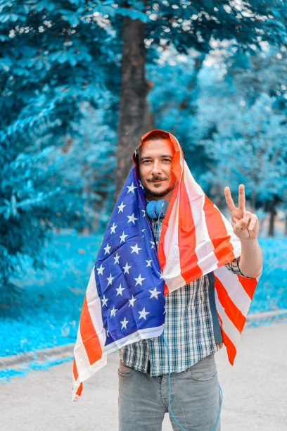 一个男人的照片背包在格子衬衫谁是走在公园和听音乐，而他是覆盖着美国国旗。图片下载