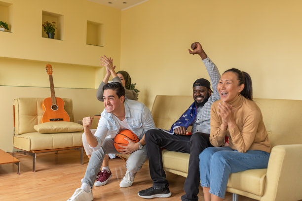 来自美国的各民族年轻朋友坐在现代公寓里观看电视上的篮球比赛图片下载