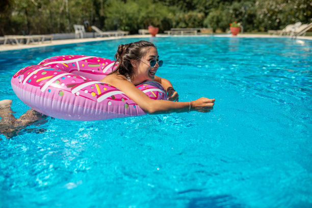 在一个炎热的夏天，一个美丽的女孩在充气甜甜圈上的游泳池里玩得很开心图片下载