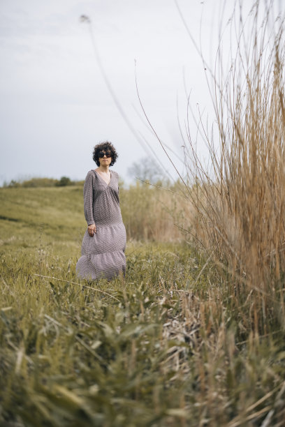 年轻的女人与卷发站在一个杂草丛生的田野，穿着长裙图片下载