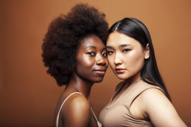 年轻漂亮的亚洲人，非洲女人摆出愉快的一起在棕色的背景，生活方式多样的民族观念图片下载