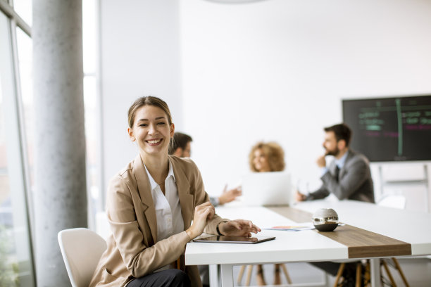 在现代办公室里，年轻的女人坐在桌子旁边，带着数字平板电脑和纸图表，在她的团队面前图片下载