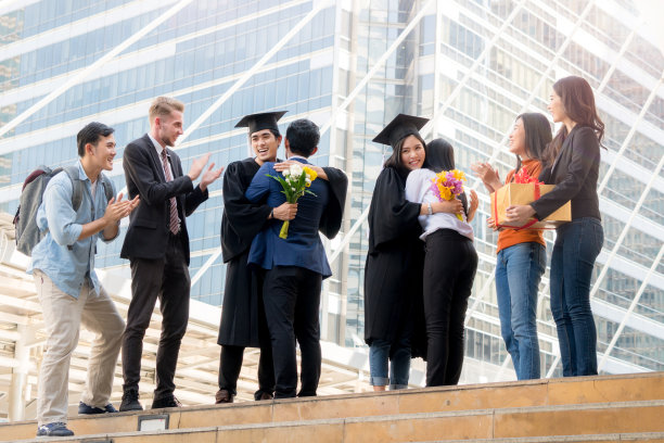 人们怀着快乐和感恩的心情，带着毕业礼服和毕业帽，与父母和朋友站在一起，在户外现代城市空间里欢快地打招呼。图片下载