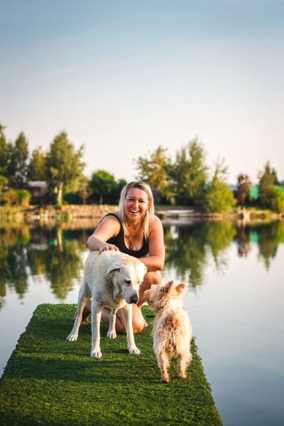 快乐的笑女人有乐趣与她的狗在码头上的湖图片下载