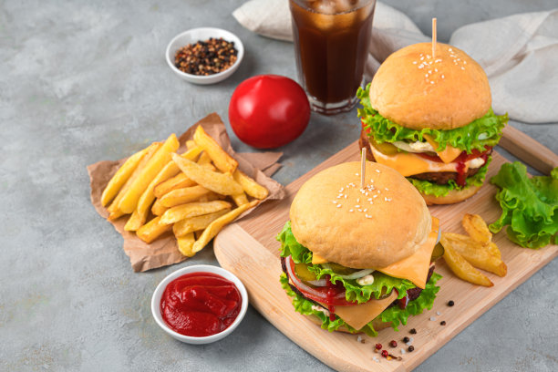 快餐，两个大汉堡加炸薯条，酱汁和可乐在灰色的背景图片下载