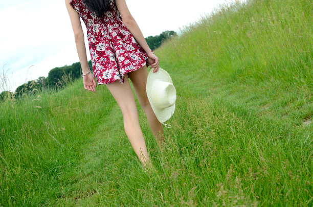 一名双腿修长的年轻女子手持夏帽在草地上行走图片下载