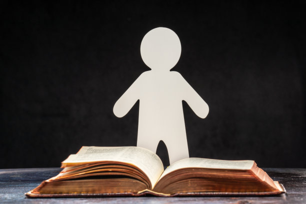 一个用纸雕刻的人站在一本打开的书前。学习和知识的概念图片下载