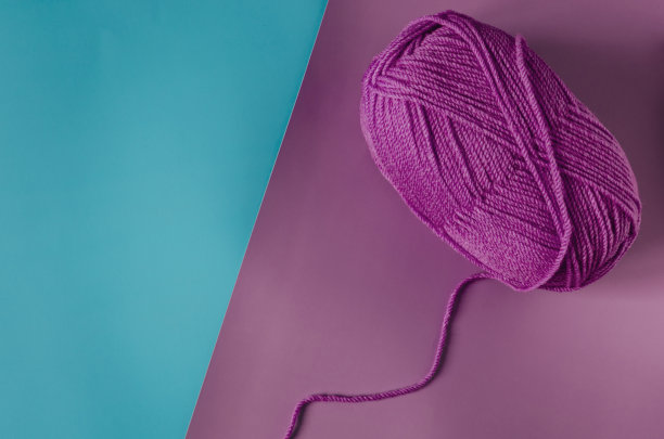 一个球的紫色纱线在一个彩色的紫绿色背景近景，针织概念。彩色纱线的细丝图片下载