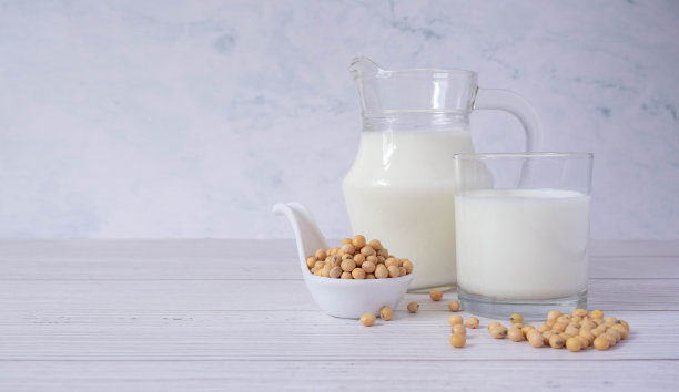 靠近美味的有机自制豆奶在玻璃和大豆或大豆在玻璃碗在木桌子的背景。豆奶是一种用大豆制成的饮料。替代牛奶和健康的概念。图片下载