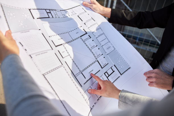 一个详细的建筑平面图或技术图纸的照片，由建筑师拿在手里用手指指向它的东西。图片下载