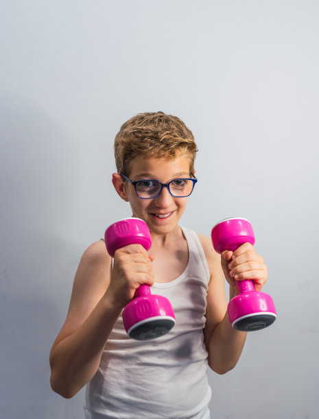 戴眼镜的金发男孩微笑着举着粉色的哑铃图片下载