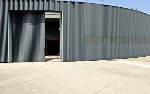 黑色的圆形墙由铝制覆层制成，前面有一大块混凝土路面。图片下载