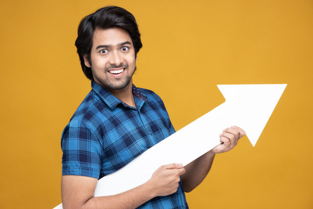 年轻男子手持箭头标志孤立在黄色背景:股票照片图片下载