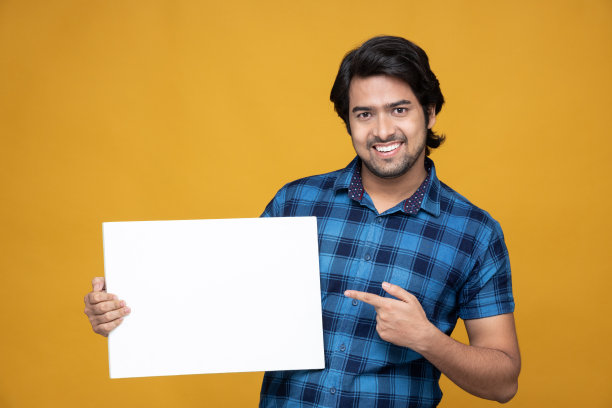 快乐的年轻人拿着一个白色广告牌孤立的黄色背景:-股票照片图片下载