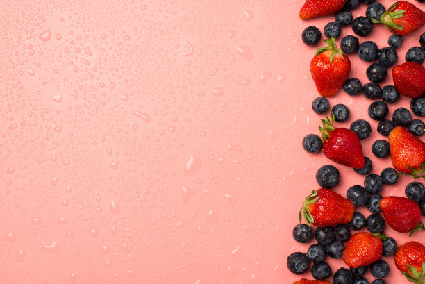 俯视图照片分散的草莓和蓝莓在右边的水滴在孤立的淡粉色背景与空白在左边图片下载