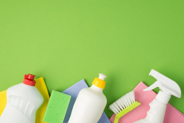 顶视图照片的白色洗涤剂瓶刷海绵和多色粘胶抹布上孤立的绿色背景与copyspace图片下载