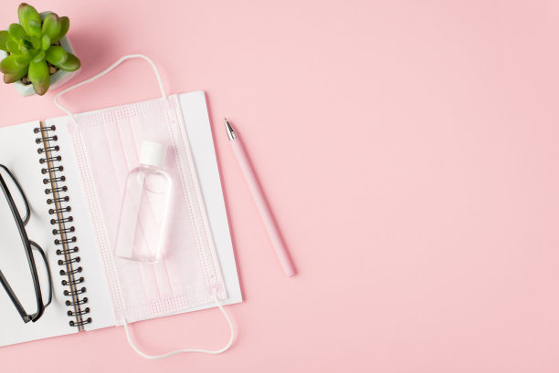 俯视图照片的粉红色医疗面罩消毒眼镜上打开的笔记本钢笔和花盆上孤立的粉色背景与copyspace图片下载