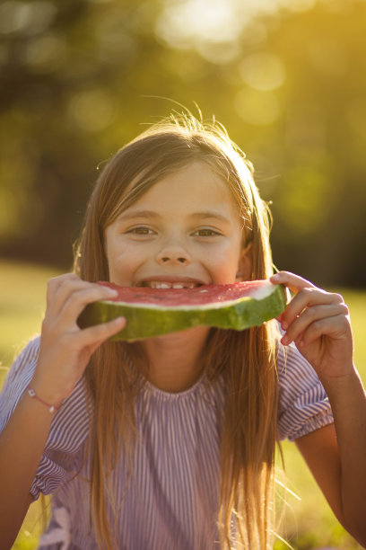 微笑的小女孩坐在大自然中吃着西瓜。看相机。享受水果。图片下载