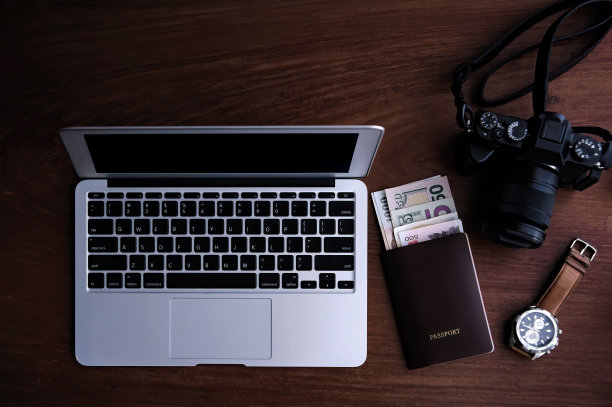 俯视图旅行摄影师与移动笔记本电脑，护照与许多钞票，数码相机和手表放在一起，在暗红色的木桌上，只聚焦于笔记本电脑图片下载