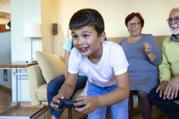 当孩子们在家里玩电子游戏的时候，一个多代同堂的家庭在周末花时间在一起。图片下载