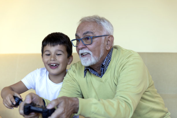 快乐的小朋友在家里玩电脑游戏的时候和爷爷玩得很开心。图片下载