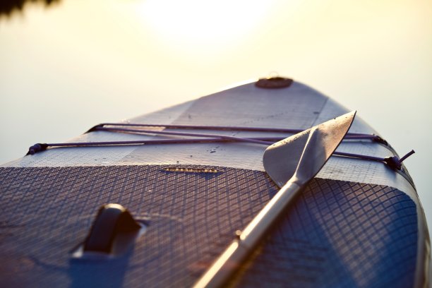 冲浪板与桨在日落的光在蓝色的水面背景接近图片下载