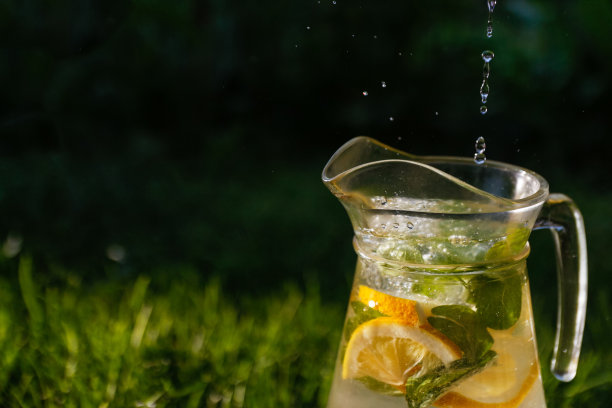 将水滴和气泡散焦，倒入装有柠檬片和薄荷叶的玻璃杯中，背景为天然绿色。一壶夏日鸡尾酒或潘趣酒。副本的空间。的焦点图片下载